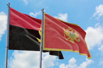 Montenegro and Angola flags waving in the wind against white cloudy blue sky together. Diplomacy...
