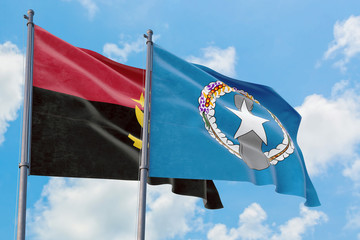 Northern Mariana Islands and Angola flags waving in the wind against white cloudy blue sky...