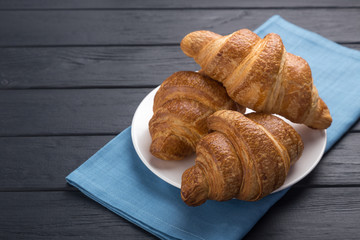 Croissants on a white plate and a black wooden table. Served with blue napkin. Fresh French Baked Croissants. Warm Fresh Buttery Rolls. Free space for text.