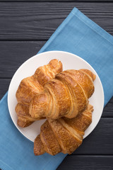 Croissants on a white plate and a black wooden table. Served with blue napkin. Fresh French Baked Croissants. Warm Fresh Buttery Rolls. Free space for text. View from above. Top view.