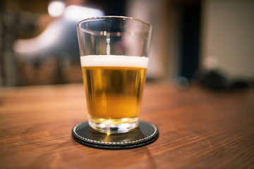 Half full pint of beer in glass on wooden bar