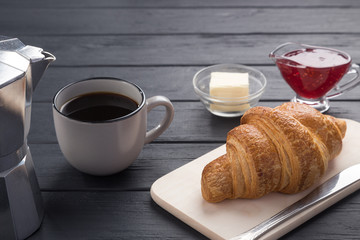 Fresh croissants on a black wooden table. Served with coffee, coffeepot, butter, jam, blue napkin. Fresh French Baked Croissants. Warm Fresh Buttery Rolls. Free space for text. 