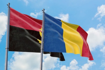 Romania and Angola flags waving in the wind against white cloudy blue sky together. Diplomacy...