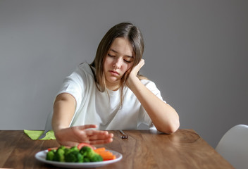 Obraz na płótnie Canvas No vegan diet concept. Teen girl pushing away plate with broccoli and other vegetables refusing to eat. Food waste. Selective focus on girl.