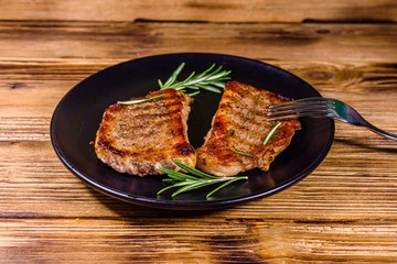 Plate with roasted steaks and rosemary twigs on a wooden table
