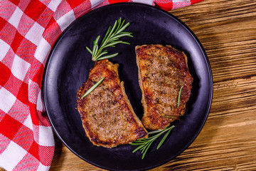 Plate with roasted steaks and rosemary twigs on a wooden table. Top view