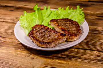 Plate with roasted steaks and rosemary twigs on a wooden table