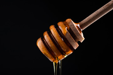  fresh honey flows from a wooden spoon for honey close-up on a black background