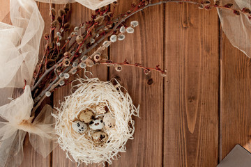 Easter quail eggs in nest and willow branch on a wooden background, copy space