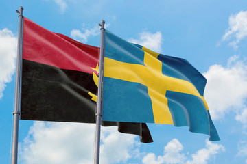 Sweden and Angola flags waving in the wind against white cloudy blue sky together. Diplomacy...