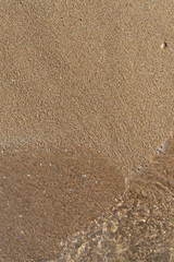 Transparent sea water covers the sandy beach shore, top view, close up. Beautiful summer vertical background with copy space