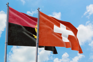 Switzerland and Angola flags waving in the wind against white cloudy blue sky together. Diplomacy...