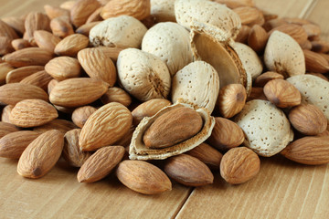 Pile of peeled raw almonds and raw almonds with shells on wooden table. Closeup