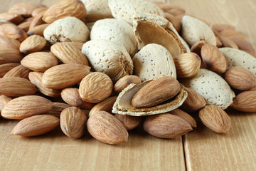 Pile of peeled raw almonds and raw almonds with shells on wooden table. Closeup