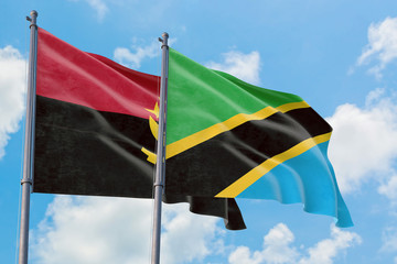 Tanzania and Angola flags waving in the wind against white cloudy blue sky together. Diplomacy concept, international relations.