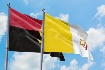 Vatican City and Angola flags waving in the wind against white cloudy blue sky together. Diplomacy...