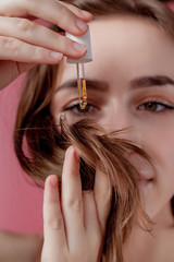 Young girl holds in her hand the tips of her hair and her right hand applies them yellow oil.