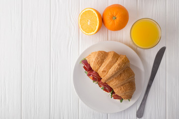 Fresh croissant sandwich with ham, cheese and arugula on white wooden table. Served with Coffee, cheese, ham, orange juice, jam. Fresh French Baked Croissants. Free space for text. View from above. To