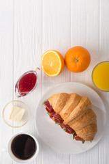 Fresh croissant sandwich with ham, cheese and arugula on white wooden table. Served with Coffee, cheese, ham, orange juice, jam. Fresh French Baked Croissants. Free space for text. View from above. To