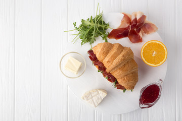 Fresh croissant sandwich with ham, cheese and arugula on white wooden table. Served with Coffee, cheese, ham, orange juice, jam. Fresh French Baked Croissants. Free space for text. View from above.