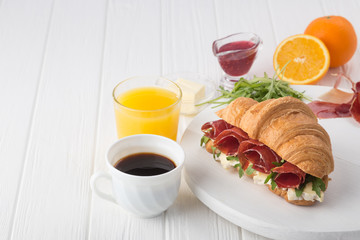 Fresh croissant sandwich with ham, cheese and arugula on white wooden table. Served with Coffee, cheese, ham, orange juice, jam. Fresh French Baked Croissants. Free space for text. 