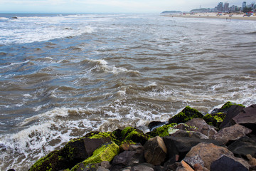 Ondas fortes na Praia dos Molhes da cidade de Torres, ao fundo a cidade abaixo de nuvens de chuva 