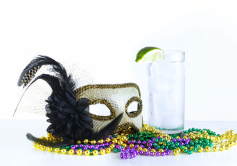 Alcoholic beverage and pourple, green and gold Mardi Gras beads with mask on a marble table for a festive February holoiday image. The drink is a Gin Fixx garnished with a lime. © Perry Correll
