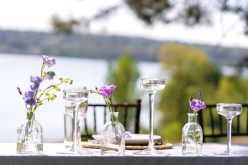 Decorative decoration of the festive table. Glass vases and fresh flowers. Decoration of holidays in the open air