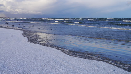 Panorama morza zimą. Zaśnieżona plaża, fale na morzu. Na niebie ciemne chmury