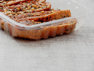 Raw uncooked pork belly slices marinated with Asian style soy souse and herbs in plastic trey on simple table cloth.