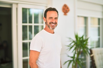 Middle age handsome man wearing casual t-shirt standing on terrace smiling
