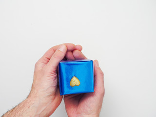 Man holding blue gift box with golden heart on top of it with two hands. Concept I love you here is my heart to you and surprise inside.