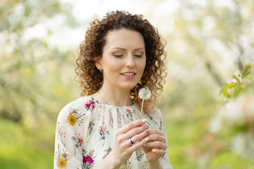 Pretty girl blowing dandelion in summer park. Green grass beautiful nature. Pure emotion.