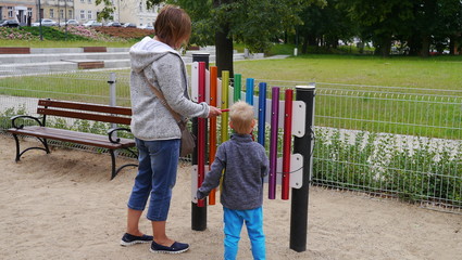 Dziecko na placu zabaw gra na cymbałkach. Stoi z mamą przy kolorowym xylophones. Chłopiec gra na...