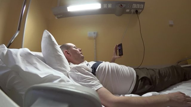 The patient looks into the smartphone lying on an anatomical bed with an electric drive. Holding the smartfnon in his left hand lifts and lowers the headboard of the bed for its convenience.