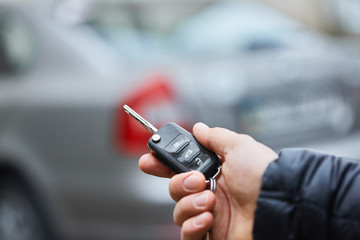 Close up hand of Man holding car key  with blurred car on background.