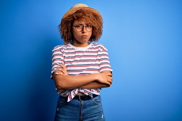 African American woman with curly hair on vacation wearing summer hat and striped t-shirt skeptic...