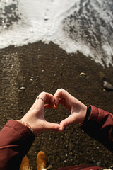 Women's hands show heart-shaped gesture amid sea waves.