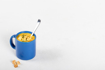 Pumpkin soup-puree with cream, wheat croutons and greens in a blue mug on a light background
