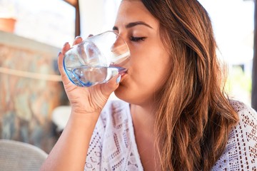 Young beautiful woman sitting at restaurant enjoying summer vacation drinking a glass of water