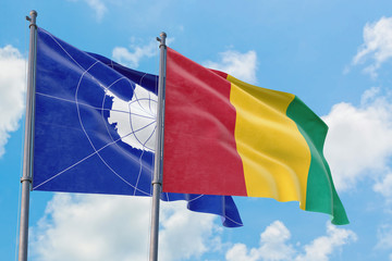 Guinea and Antarctica flags waving in the wind against white cloudy blue sky together. Diplomacy concept, international relations.