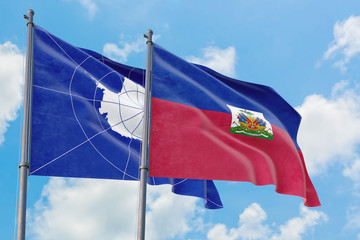 Haiti and Antarctica flags waving in the wind against white cloudy blue sky together. Diplomacy concept, international relations.