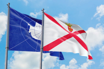 Jersey and Antarctica flags waving in the wind against white cloudy blue sky together. Diplomacy concept, international relations.