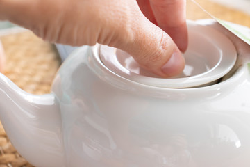 A female hand opening a lid of a ceramic pot with brewed traditional tea in a restaurant