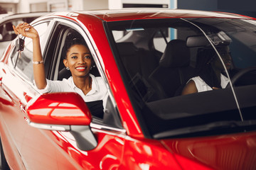 Women buying the car. Ladies in a car salon. Black girls near red car