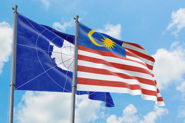 Malaysia and Antarctica flags waving in the wind against white cloudy blue sky together. Diplomacy concept, international relations.