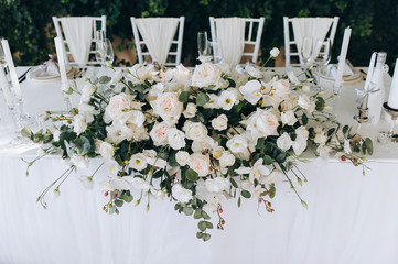 A wedding table with a white tablecloth, candles, a large bouquet of white roses and vintage chairs...