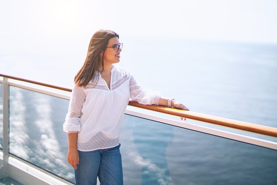Young beautiful woman on vacation smiling happy and confident. Standing on a deck of ship with smile on face doing a cruise