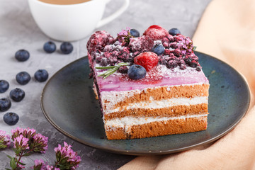 Berry cake with milk cream and blueberry jam on blue ceramic plate with cup of coffee and fresh blueberries on a gray concrete background with orange textile. side view, selective focus