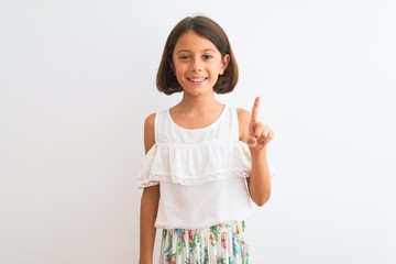 Young beautiful child girl wearing casual dress standing over isolated white background showing and pointing up with finger number one while smiling confident and happy.